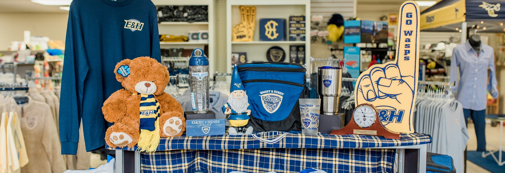 various merchandise for sale in the store including a teddy bear, a clock, a garden gnome,a cup, water bottle and travel mug, a cooler, a foam finger and a long sleeve blue t-shirt.